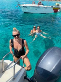 A group of friends enjoys a refreshing swim in crystal-clear waters, with a boat anchored nearby, capturing the essence of a perfect summer day on the water.