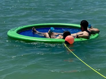 A couple relaxes on a floating mat in the water, enjoying drinks and the sun — a perfect way to unwind during a day on the water.