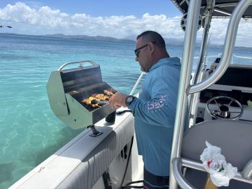 A chef grills delicious food on a boat, showcasing the perfect onboard BBQ experience amidst stunning turquoise waters.