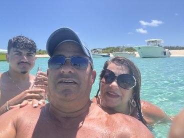 A joyful group enjoys a refreshing swim in crystal-clear waters, capturing a fun moment with drinks in hand — perfect for a beach day adventure.