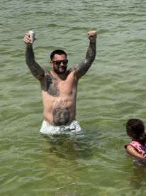 A man celebrates in the water with a drink, while a child enjoys the fun nearby — capturing the essence of a lively day on the water.