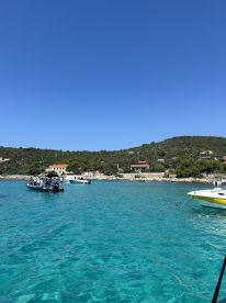 A picturesque view of boats anchored in crystal-clear waters, surrounded by lush greenery and charming coastal homes — a perfect setting for a relaxing day on the water.