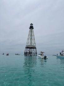 A picturesque view of a lighthouse surrounded by boats in clear turquoise waters, showcasing a popular destination for boating enthusiasts.