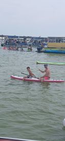 A father and son enjoy paddleboarding together in a lively waterway, surrounded by other groups having fun — a perfect family adventure on the water.