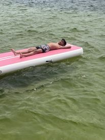A young boy relaxes on a pink floating mat in clear waters, enjoying a sunny day — a perfect scene for summer fun and water activities.
