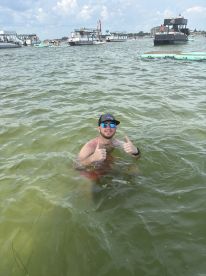 A man enjoys a fun day swimming in the water, giving a thumbs up amidst a lively backdrop of boats — perfect for summer adventures and water activities.