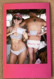 A joyful couple celebrates a marriage proposal on a boat, showcasing their excitement with playful signs — a perfect moment for romantic adventures on the water.