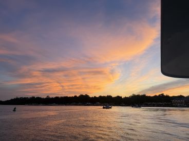 A stunning sunset over the water, showcasing vibrant colors and a tranquil coastline — perfect for capturing the beauty of evening boat trips.