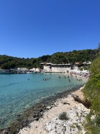A vibrant beach scene with groups of people enjoying the clear waters and sunny weather, perfect for a day of relaxation and fun by the coastline.