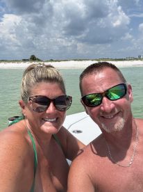 A cheerful couple takes a selfie on a boat, enjoying a sunny day at the beach — perfect for capturing memorable moments on the water.