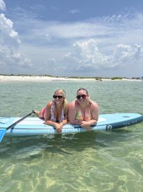 Two friends enjoy paddleboarding in clear waters, showcasing a perfect beach day filled with fun and relaxation.