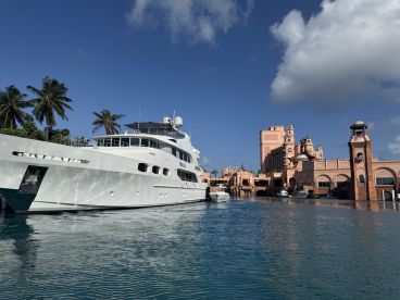 A stunning yacht docked near the iconic Atlantis resort, showcasing luxury and elegance against a backdrop of palm trees and clear blue skies.
