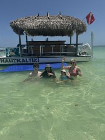 A cheerful group enjoys a fun day at the sandbar, swimming and relaxing near the Nautical Tiki boat — a perfect setting for memorable moments on the water.