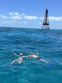 A couple enjoys snorkeling in vibrant turquoise waters, playfully posing with a lighthouse in the background — a perfect snapshot of adventure and fun on the water.