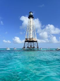 A stunning view of a historic lighthouse surrounded by turquoise waters, with boats nearby, perfect for capturing the essence of a beautiful day on the water.
