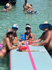 A lively group enjoys a fun day at the sandbar, relaxing in the water with drinks and games — the perfect setting for a summer getaway.