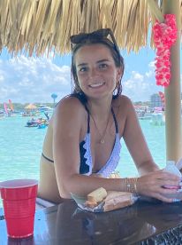 A smiling woman enjoys refreshments at a beachside bar, capturing the essence of a fun day on the water with friends.