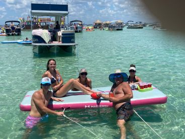 A lively group enjoys a fun day on a floating mat in crystal-clear waters, perfect for summer parties and relaxation.