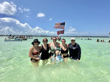 A joyful group of friends and family enjoys a sunny day at the beach, swimming in clear waters with jet skis in the background — a perfect summer getaway.