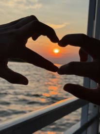 A romantic moment captured as a couple forms a heart shape with their hands against a stunning sunset backdrop on the water, perfect for celebrating love and special occasions.