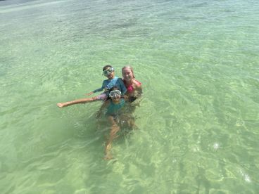 A joyful group of children and an adult enjoy snorkeling in crystal-clear waters, making for a perfect family adventure in a tropical paradise.