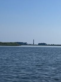 A serene view of a lighthouse standing tall against a clear blue sky, surrounded by tranquil waters — a picturesque scene perfect for boating adventures.