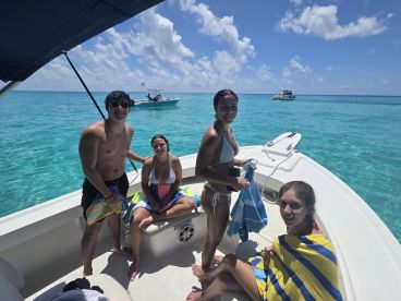 A group of friends enjoys a sunny day on the water, relaxing on a boat with vibrant turquoise waters in the background — perfect for summer adventures and fun outings.