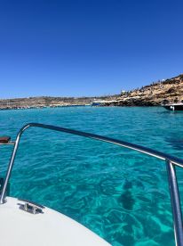 A stunning view from a boat showcasing the vibrant turquoise waters and rocky coastline, with people enjoying the beach and water activities in the background.