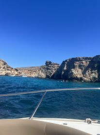A stunning view of a rocky coastline with swimmers in the clear blue waters, showcasing the beauty of a boat trip along the coast.