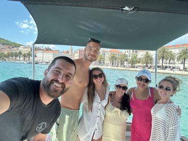 A cheerful group poses for a selfie on a boat with a picturesque waterfront backdrop, perfect for memorable outings and celebrations.