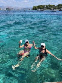 Two friends enjoy a refreshing swim in crystal-clear waters, sipping drinks and soaking up the sun — a perfect moment for summer fun and relaxation.