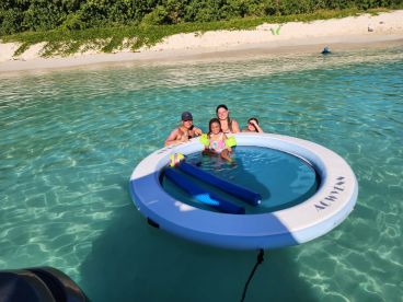 A joyful family enjoys a sunny day in the water, playing on a floating mat — a perfect beach experience for fun and relaxation.