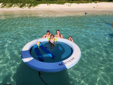 A joyful family enjoys a sunny day in the water, relaxing on a floating mat with colorful pool toys — a perfect moment for summer fun and family bonding.