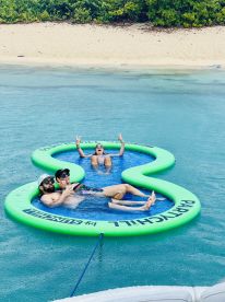 A fun group enjoys a floating mat in crystal-clear waters, perfect for relaxation and summer parties. Ideal for social gatherings and water activities.