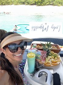 A woman enjoys a colorful spread of snacks and drinks on a boat, perfect for a relaxing day on the water.