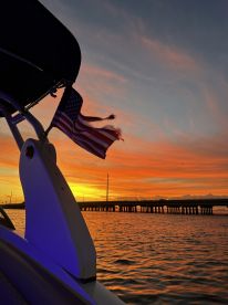 A stunning sunset view featuring a boat's silhouette with an American flag waving, creating a picturesque scene perfect for evening cruises.