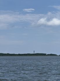 A scenic view of a lighthouse standing tall on an island, surrounded by calm waters and a clear blue sky — a perfect representation of coastal beauty.