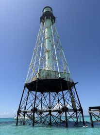 A stunning view of a lighthouse standing tall over clear turquoise waters, with snorkelers exploring the vibrant marine life nearby — a perfect destination for water adventures.