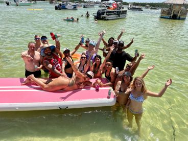 A lively group enjoys a fun day in the water, celebrating on a paddleboard with drinks in hand — perfect for summer parties and memorable outings.