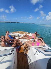 A lively group of friends enjoys a sunny day on the boat, relaxing and sunbathing in vibrant swimsuits — perfect for a fun day out on the water.
