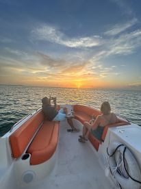 A couple enjoys a romantic sunset on a boat, capturing the moment with their phones — an ideal setting for memorable cruises.