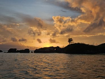 A stunning sunset over a serene island coastline, creating a picturesque backdrop perfect for romantic getaways or tranquil boat trips.