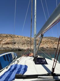 A person relaxes on the deck of a sailboat with a paddleboard nearby, enjoying a sunny day on the water — perfect for leisurely sailing adventures.