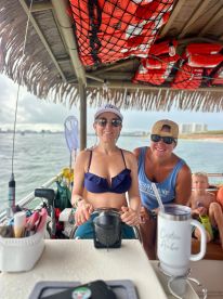 Two friends enjoy a fun moment at the helm of a boat, showcasing the excitement of a day on the water with a child in the background.
