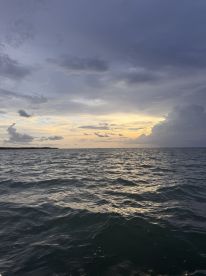 A serene view of the ocean under a cloudy sky at sunset, creating a tranquil atmosphere.