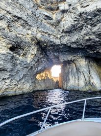 A stunning view of a natural rock formation with a boat navigating through a cave, showcasing the beauty of coastal scenery.