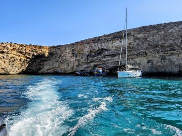 A picturesque view of a sailboat anchored near a rocky cliff, showcasing the stunning turquoise waters and natural beauty of the coastline.