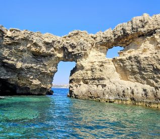 A stunning view of a natural rock arch along the coastline, showcasing the beautiful turquoise waters — a perfect destination for boat tours and scenic adventures.