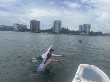 Two friends enjoy a playful moment in the water, reaching for a frisbee during a fun day out on the boat — perfect for summer adventures.