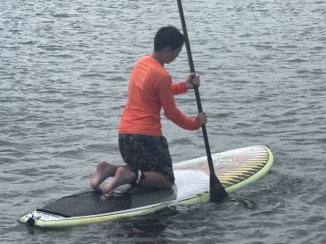 A young boy kneels on a paddleboard, navigating the calm waters, showcasing the fun and adventure of water sports.